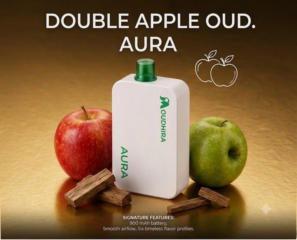 A white AURA diffuser bottle with a green cap stands on a warm brown surface, flanked by a red apple, a green apple, and cinnamon sticks. Large text at the top reads 'DOUBLE APPLE OUD.