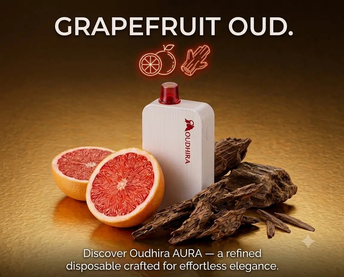 A white Oudhira AURA disposable vape device with a red mouthpiece, styled with sliced grapefruit and dried botanicals on a warm brown background. The text 'GRAPEFRUIT OUD.