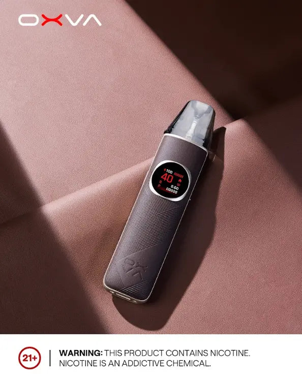 An OXVA electronic nicotine pouch device with a digital display, resting on a textured dusty rose surface with dramatic shadows. A white banner at the bottom contains a 21+ warning and text stating nicotine is an addictive chemical. Order now and get FREE DELIVERY