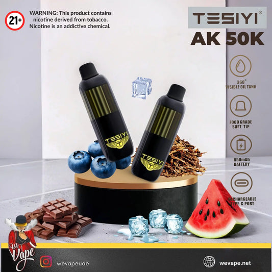Two black TESIYI AK 50K disposable vape devices with gold accents, displayed on a black and gold pedestal with blueberries, chocolate, ice, and a slice of watermelon. 